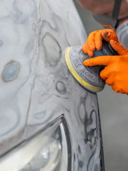 A mechanic sands the putty on a car body with a machine. Repair after an accident. Vertical photo