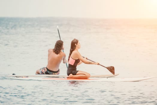 Sea woman and man on sup. Silhouette of happy young woman and man, surfing on SUP board, confident paddling through water surface. Idyllic sunset. Active lifestyle at sea or river