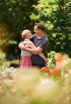 Happy, hug and couple in a park with love, trust and support, solidarity and security while bonding in nature. Commitment, care and people embrace on a field of flowers for spring romance or date.