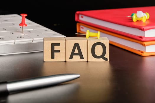 FAQ TEXT the text of non-wooden cubes next to notepads, a calculator, a pen on a black background