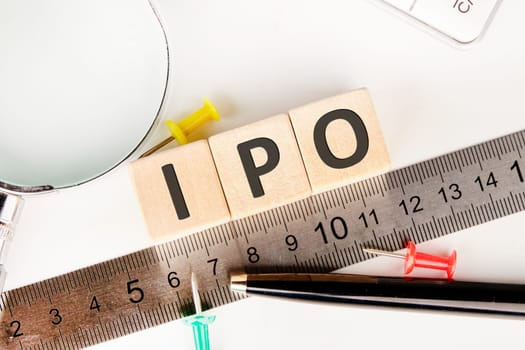 IPO abbreviation of Initial Public Offering text of non-wooden cubes next to a calculator, pen, measuring ruler, magnifying glass on a white background