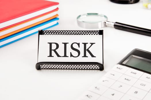 RISK text on a business card next to office supplies on a white background