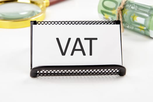 VAT the text on the business card next to the roll of money with a magnifying glass in the background is out of focus on a white background