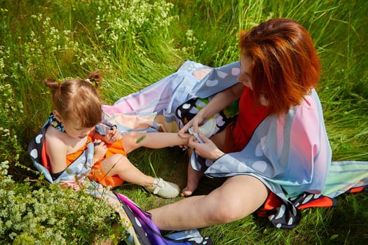 Happy female family with mother and daughter on green and yellow meadow full of grass and flower. Woman with red hair and blonde girl having fun, joy and hug in sunny summer day. Concept family love