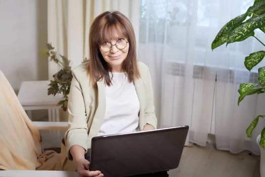 Elderly lady with glasses and laptop in room. Businesswoman is leader, manager working online. Blogger streaming. Grandma with family on Internet