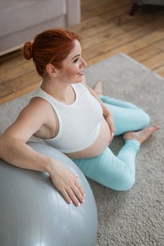 Pregnant woman resting after workout sitting on the floor near the fitness ball