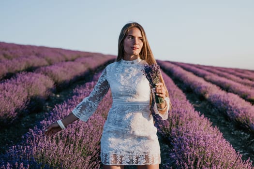 Close up portrait of young beautiful woman in a white dress and a hat is walking in the lavender field and smelling lavender bouquet.