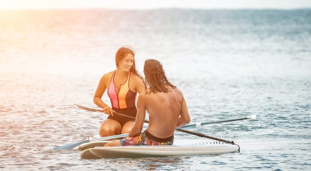 Sea woman and man on sup. Silhouette of happy young woman and man, surfing on SUP board, confident paddling through water surface. Idyllic sunset. Active lifestyle at sea or river