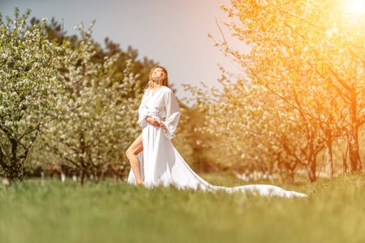 Blond blooming garden. A woman in a white dress walks through a blossoming cherry orchard. Long dress flies to the sides