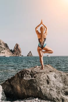 Yoga on the beach. A happy woman meditating in a yoga pose on the beach, surrounded by the ocean and rock mountains, promoting a healthy lifestyle outdoors in nature, and inspiring fitness concept