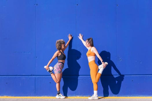 two sportswomen stretching together outdoors in a sunny day, concept of friendship in sport and active lifestyle, copy space for text