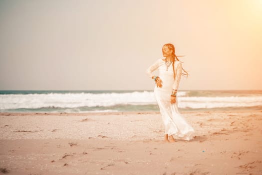 woman sea white dress. Model in boho style in a white long dress and silver jewelry on the beach. Her hair is braided, and there are many bracelets on her arms