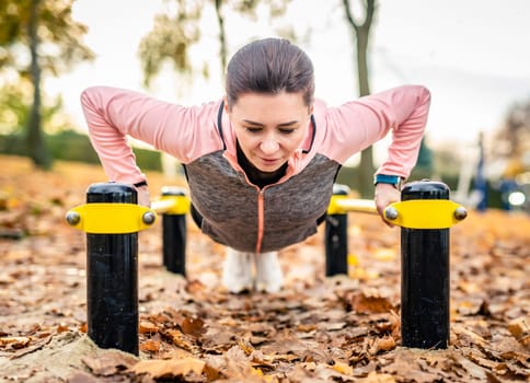 Fitness girl doing push ups outdoots in autumn time. Young woman exercising in park
