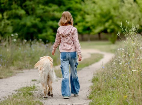 Preteen girl with golden retriever dog walking at nature. Cute child kid with purebred pet doggy labrador in park at summer