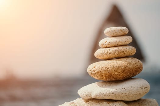 Pyramid stones on the seashore with warm sunset on the sea background. Happy holidays. Pebble beach, calm sea, travel destination. Concept of happy vacation on the sea, meditation, spa, calmness.