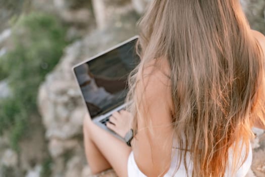 Freelance women sea working on the computer. Good looking middle aged woman typing on a laptop keyboard outdoors with a beautiful sea view. The concept of remote work