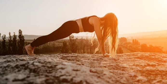 Well looking middle aged woman with long hair, fitness instructor in leggings and tops doing stretching and pilates on the rock near forest. Female fitness yoga routine concept. Healthy lifestyle.