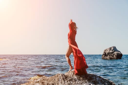 Woman travel sea. Young Happy woman in a long red dress posing on a beach near the sea on background of volcanic rocks, like in Iceland, sharing travel adventure journey