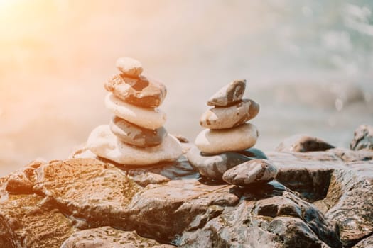 Pyramid stones on the seashore with warm sunset on the sea background. Happy holidays. Pebble beach, calm sea, travel destination. Concept of happy vacation on the sea, meditation, spa, calmness.