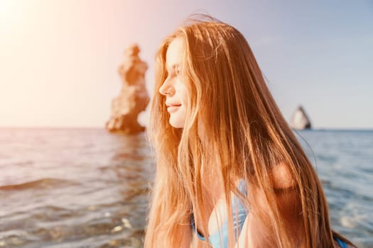 Close up shot of happy young caucasian woman looking at camera and smiling. Cute woman portrait in bikini posing on a volcanic rock high above the sea