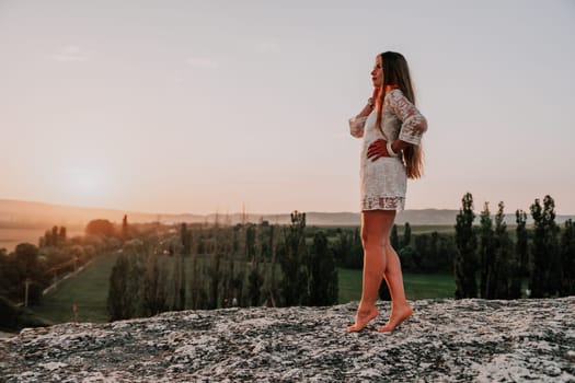 Romantic beautiful bride in white dress posing with sea and mountains in background. Stylish bride standing back on beautiful landscape of sea and mountains on sunset