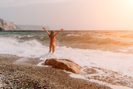 Woman travel sea. Young Happy woman in a long red dress posing on a beach near the sea on background of volcanic rocks, like in Iceland, sharing travel adventure journey