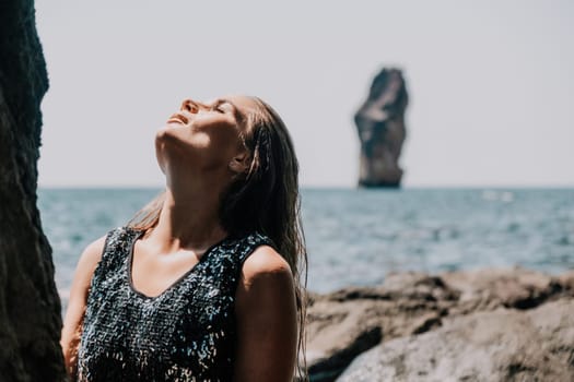 Woman travel sea. Young Happy woman in a long red dress posing on a beach near the sea on background of volcanic rocks, like in Iceland, sharing travel adventure journey