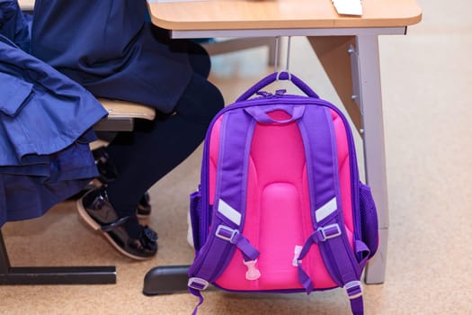 The school backpack hangs on a hook at the desk where the student sits. High quality photo