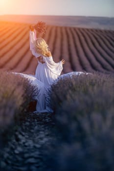 Blonde woman poses in lavender field at sunset. Happy woman in white dress holds lavender bouquet. Aromatherapy concept, lavender oil, photo session in lavender.