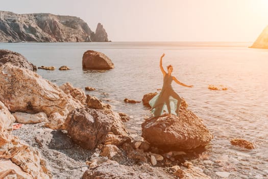 Woman green dress sea. Woman in a long mint dress posing on a beach with rocks on sunny day. Girl on the nature on blue sky background