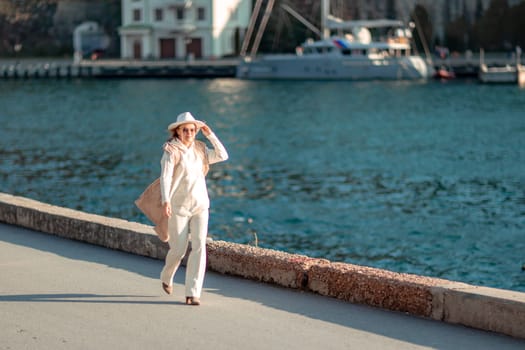 Happy blonde woman in a white suit and hat posing at the camera against the backdrop of the sea.