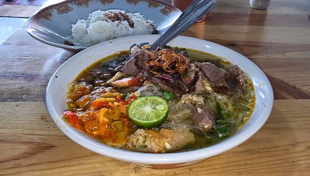 Indonesian style beef noodle soup called soto mie, freshly made soup with vermicelli rice noodle, fried shallots, chilli paste, and fried rissoles and fresh lime juice