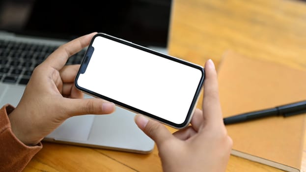 Young woman watching videos or playing video games on smartphone at wooden desk.