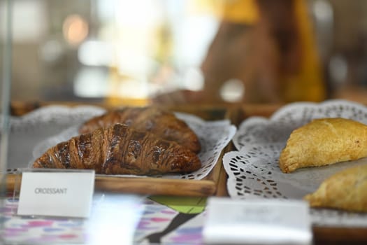 Freshly baked chocolate croissants and pies in glass showcase at bakery.