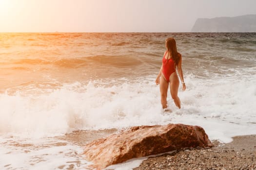 Woman travel sea. Young Happy woman in a long red dress posing on a beach near the sea on background of volcanic rocks, like in Iceland, sharing travel adventure journey