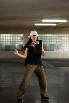 Cheerful young woman dancing in style of hip hop aesthetics in parking garage.