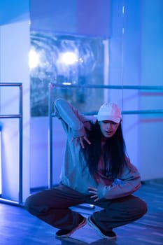 Portrait of young woman practicing modern hip hop dance in studio with neon lights.