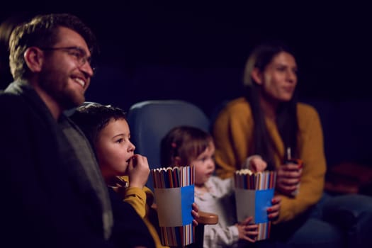 A modern family enjoys quality time together at the cinema, indulging in popcorn while watching a movie with their children.