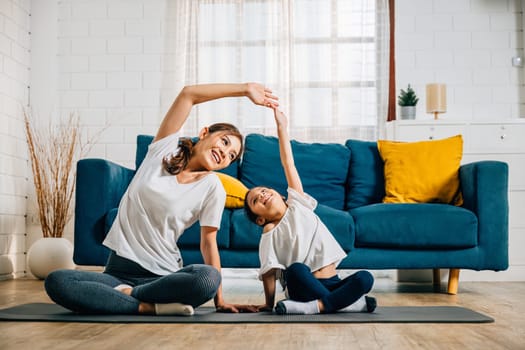 An Asian mother teaches her daughter yoga focusing on posture and balance. Their smiles reflect a happy family moment filled with relaxation vitality and togetherness at home.