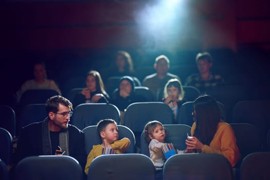 A modern family enjoys quality time together at the cinema, indulging in popcorn while watching a movie with their children.