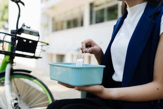 Asian young businesswoman bike to work for eco friendly green energy and eat lunch using box lunch prepared from home. while commuting in city. Eco friendly.