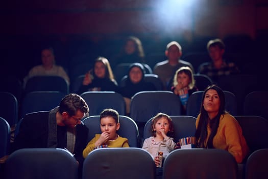 A modern family enjoys quality time together at the cinema, indulging in popcorn while watching a movie with their children.