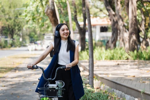 Asian young businesswoman bike to work for eco friendly green energy and listen music with headphone while commuting in city. Eco friendly.