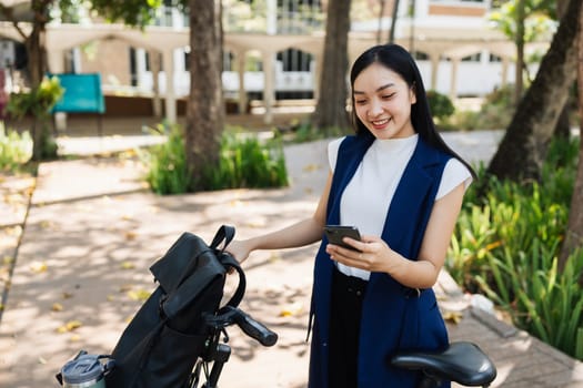 Asian young businesswoman bike to work for eco friendly green energy and use smart phone while commuting in city. Eco friendly.