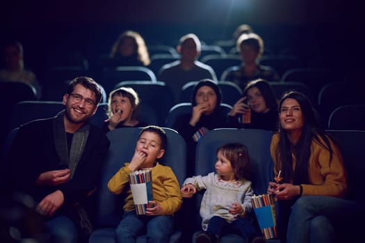 A modern family enjoys quality time together at the cinema, indulging in popcorn while watching a movie with their children.