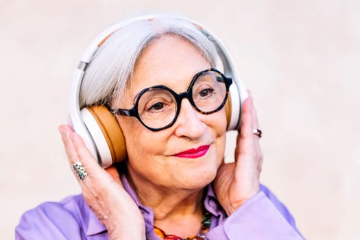 smiling senior woman in glasses listening to music in her headphones, concept of elderly people leisure and active lifestyle
