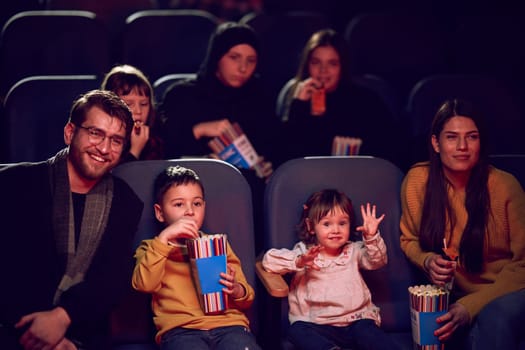 A modern family enjoys quality time together at the cinema, indulging in popcorn while watching a movie with their children.