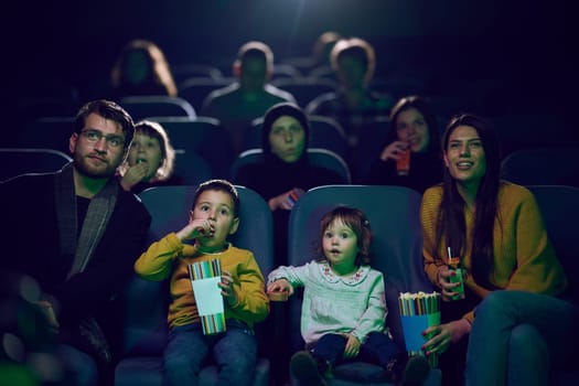 A modern family enjoys quality time together at the cinema, indulging in popcorn while watching a movie with their children.