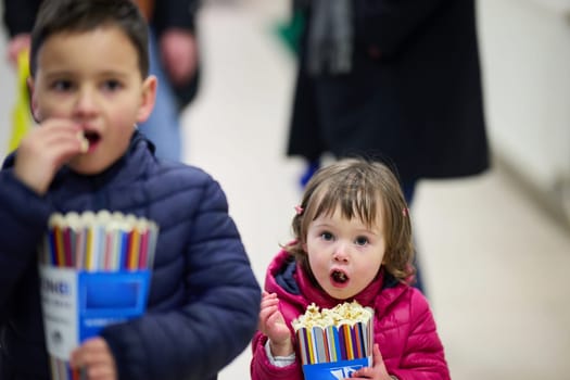 A brother and his younger sister joyfully share a bag of popcorn as they head to the cinema together to watch a movie, embodying the warmth of sibling bond and anticipation for the film ahead.