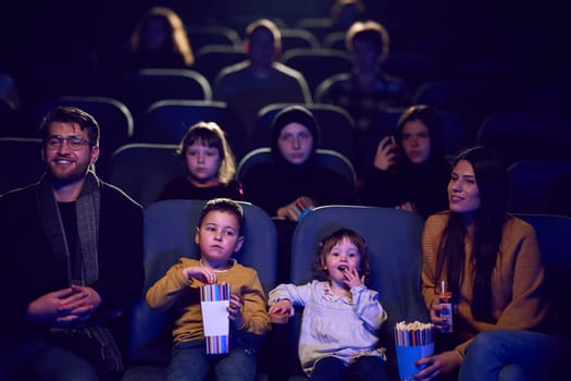 A modern family enjoys quality time together at the cinema, indulging in popcorn while watching a movie with their children.